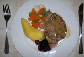 Stekt fläskkotlett med gröna ärtor, morötter och svartvinbärsgelé.